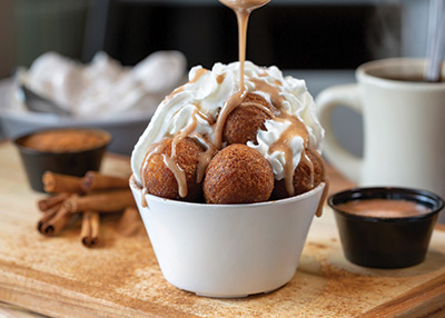 bowl of donut holes with whipped cream and sauce drizzling on top